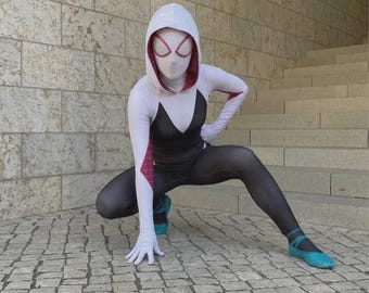 Op de afbeelding: Een volledig spandex pak met een witte capuchon met roze binnenkant, een zwart rompgedeelte en witte mouwen met roze webpatronen. Het pak bevat een wit volgelaatsmasker met grote roze omrande ooglenzen en blauwgroene ballerina's.