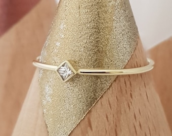 May include: A delicate gold ring with a single, clear square-shaped gemstone.