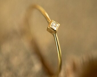 May include: A delicate gold ring with a small square-shaped diamond.