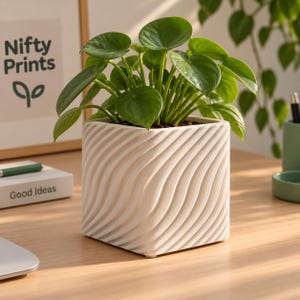 Op de afbeelding: Een vierkante witte keramische plantenpot met een gestructureerd diagonaal golfpatroon op de buitenkant. De pot bevat een weelderige groene plant met ronde, hartvormige bladeren die vanuit het midden van de pot naar buiten toe groeien.