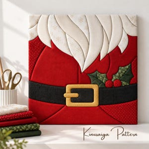 May include: A square fabric wall art piece featuring a Kimekomi-style Santa Claus design with a white beard, red coat, black belt with a gold buckle, and green holly leaves with red berries. The text Kinusaiga Pattern is visible below.