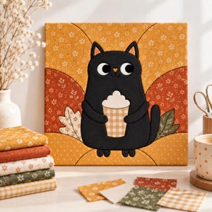 May include: A square fabric wall art piece featuring a black cat holding a beige and white checkered cup with foam. The background consists of curved panels in mustard yellow and burnt orange with white floral patterns and leaf motifs.