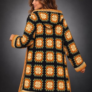 May include: A long-sleeved hooded cardigan constructed from black, orange, olive green, and cream-colored granny square crochet motifs. The garment features a hood, long sleeves with ribbed cuffs, and a straight hemline finished with a solid orange border.