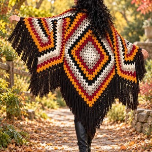 May include: A crochet poncho featuring a diamond-shaped granny square pattern in shades of black, white, mustard yellow, and deep red. The garment is finished with long black fringe along the edges, creating a textured, layered appearance.