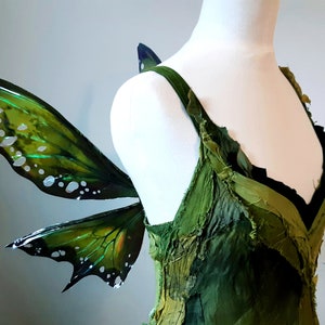 May include: Green fairy wings with iridescent details and a white, green, and black dress.