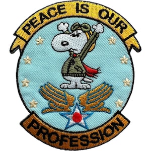 May include: A circular embroidered patch featuring a light blue background with white stars. A white cartoon dog wearing a green flight jacket and aviator cap stands above gold wings and a star emblem. The yellow border reads PEACE IS OUR PROFESSION.