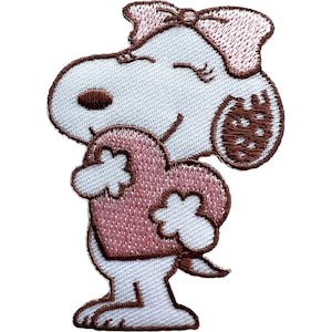 May include: An embroidered iron-on patch featuring a white cartoon dog with a brown nose and ear, wearing a pink bow on its head. The dog is holding a large pink heart against its chest with both paws, with eyes closed in a happy expression.