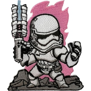 May include: An embroidered patch featuring a stylized white armored soldier holding a large weapon with a blue energy beam. The figure stands on a gray rocky surface against a vibrant pink flame-like background, rendered in detailed thread work.