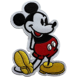 May include: An embroidered patch featuring the classic cartoon character Mickey Mouse. The character has a white face, black ears, a black shirt, red shorts, and large yellow shoes. The entire design is outlined with a thick white border.