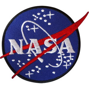May include: A circular embroidered patch featuring a blue background with white stars and a white curved orbital path. The text NASA is stitched in white across the centre, intersected by a bold red swooping vector shape with a black border.