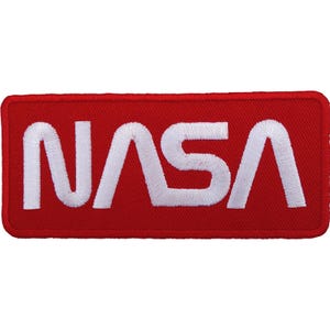 Op de afbeelding: Een rechthoekige geborduurde patch met een felrode achtergrond en het woord NASA in dikke witte letters gestikt. De patch heeft afgeronde hoeken en een bijpassende rode gestikte rand, wat zorgt voor een strakke en gedefinieerde afwerking.
