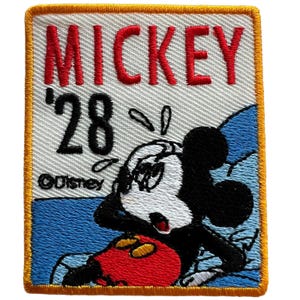 May include: A rectangular embroidered patch featuring Mickey Mouse in a red, black, and white design. The text MICKEY and '28 are stitched in red and black thread respectively. The Disney logo is visible in black on a white background.