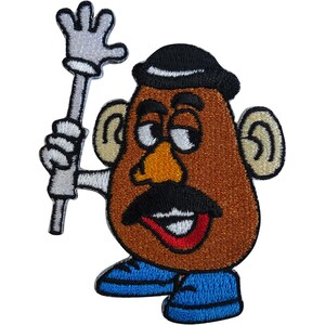 Puede incluir: Un parche bordado que muestra un personaje marrón con forma de patata, con un bombín negro, nariz amarilla, bigote negro y boca roja. El personaje tiene orejas de color beige, zapatos azules y una mano con guante blanco sosteniendo un bastón.