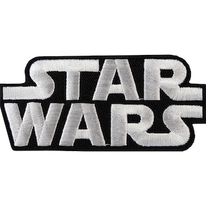 May include: A rectangular embroidered patch featuring the words STAR WARS in a bold, stylised white font. The letters are stitched with a dense white thread against a solid black background, creating a high-contrast design with a textured finish.