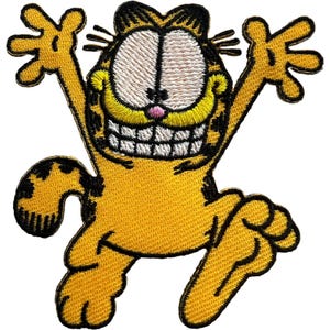 Puede incluir: Un parche bordado que representa al personaje de dibujos animados Garfield, ilustrado en una paleta de colores amarillo y naranja vibrantes con rayas negras. El personaje se muestra con los brazos levantados, una amplia sonrisa.