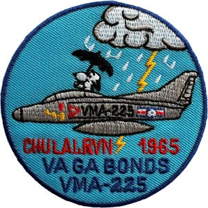 Può includere: Una toppa ricamata circolare con sfondo azzurro raffigurante un aereo da caccia grigio, un personaggio dei cartoni animati con un ombrello nero sotto una nuvola bianca con un fulmine giallo e il testo CHULALRVN 1965 VA GA BONDS VMA-225.