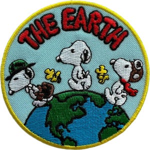 May include: A circular embroidered patch featuring a light blue background with the text THE EARTH in red. Three white cartoon dogs are depicted on top of a green and blue globe. One dog wears a green hat, one is plain, and one wears a brown aviator cap.