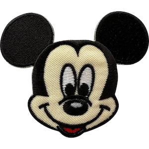 May include: An embroidered iron-on patch featuring the iconic head of Mickey Mouse. The design displays black ears, a cream-colored face, white eyes with black pupils, a black nose, a curved black smile, and a small red tongue visible at the bottom.