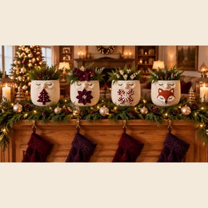 Könnte beinhalten: Vier cremefarbene gehäkelte Töpfe mit Gesichtern mit geschlossenen Augen, die jeweils Grünpflanzen enthalten. Die Töpfe haben verschiedene Applikationen: einen roten Weihnachtsbaum, einen dunkelroten Weihnachtsstern, eine Zuckerstange und ein Fuchskopf.