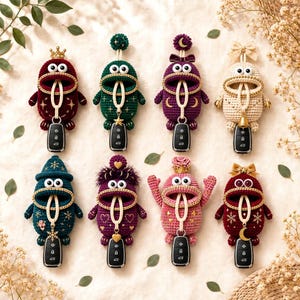 May include: Eight crocheted monster-shaped key covers in various colors including red, green, purple, cream, teal, and pink. Each features large white eyes, a wide open mouth holding a car key fob, and unique decorative accents like crowns, bows, stars, and moons.