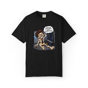 May include: A black short-sleeve t-shirt featuring a graphic of a skeleton with brown hair and glasses sitting on the floor near a server rack. The skeleton has a speech bubble that reads, SHOULD'VE WAITED UNTIL AFTER BUSINESS HOURS.
