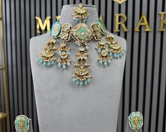 May include: A gold-toned necklace and earring set featuring light blue and peach enamel accents, clear stones, and dangling light blue beads. The necklace includes a central pendant with a matching smaller piece above it and hanging charms.
