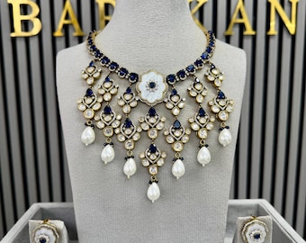 May include: A necklace and earring set featuring dark blue stones and white pear-shaped pearls. The necklace has a multi-layered design with floral-shaped accents, clear crystals, and dark blue stones set in a metallic frame. Matching earrings.
