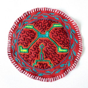 May include: A circular red fabric patch with a white stitched border. The center of the patch features a colorful geometric design with green, blue, orange, and pink embroidery.
