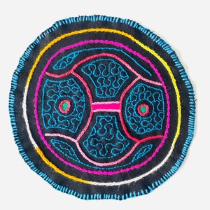 May include: A circular embroidered patch with a black background and colorful geometric designs. The design features concentric circles in yellow, pink, and blue, with a central motif of overlapping shapes in blue, pink, and green.