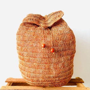 May include: A brown woven bag with two wooden beads on the front. The bag is sitting on a wooden crate.