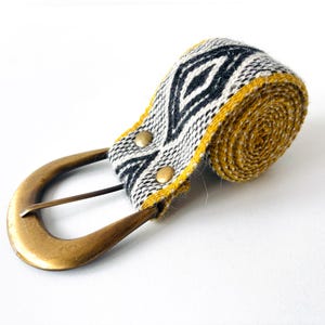 May include: A woven belt with a black, white, and yellow geometric pattern. The belt has a brass buckle.