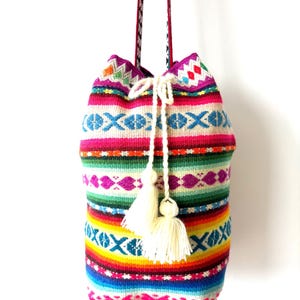 Może przedstawiać: Kolorowa tkana torba typu kubełek ze sznurkiem do ściągania w kolorze białym i frędzlami. Torba ma geometryczny wzór w odcieniach różowego, niebieskiego, zielonego, żółtego i pomarańczowego.