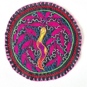 May include: A circular embroidered patch with a black background and a pink, blue, yellow, and orange floral design. The patch is surrounded by a pink, red, green, and black border.
