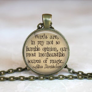 Op de afbeelding: Een bronzen ketting met een ronde glazen hanger met een citaat van Albus Perkamentus: "Woorden zijn, naar mijn bescheiden mening, onze meest onuitputtelijke bron van magie."