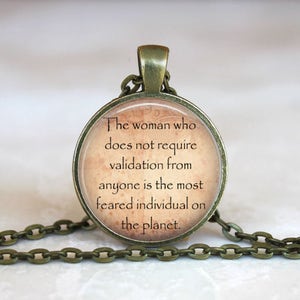 May include: A bronze necklace with a round pendant featuring a quote: "The woman who does not require validation from anyone is the most feared individual on the planet."