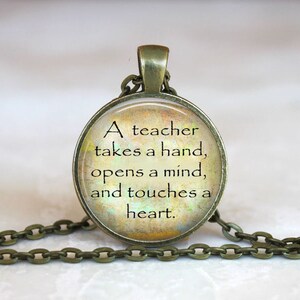 May include: A bronze necklace with a round glass pendant featuring a quote about teachers: "A teacher takes a hand, opens a mind, and touches a heart."