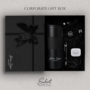 May include: A black corporate gift box featuring a black ribbon and bow, containing a black tumbler with the text Your Logo Here, a black pen, a white earbud case with the text Your Logo Here, and a black charging cable with a circular tag.