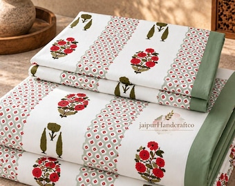 Può includere: Un set di lenzuola in cotone bianco piegato con un motivo ripetuto di fiori rossi e sagome di alberi verdi, separati da fasce di piccole forme geometriche rosse e verdi, con un bordo verde salvia e il testo jaipurHandcraftco.