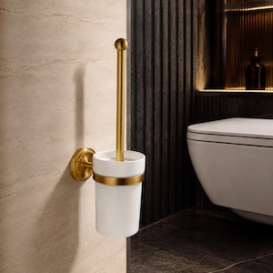 May include: A wall-mounted toilet brush holder featuring a white cylindrical ceramic container with a brushed gold metal band. The matching gold metal handle has a spherical top and is secured to the wall by a circular gold base.