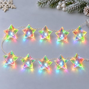 May include: A string of ten translucent, iridescent star-shaped lights connected by a thin wire. Each star features a faceted surface that reflects a spectrum of colors, with a bright white LED light glowing from the center of each individual star.
