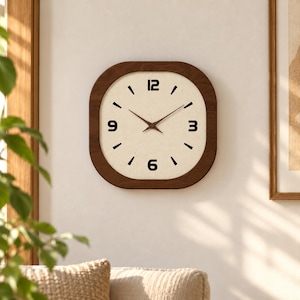 May include: A square wall clock with rounded corners, featuring a dark brown wooden frame and a cream-colored face. The clock has black numerals at the 12, 3, 6, and 9 o'clock positions, with black tick marks for the remaining hours.