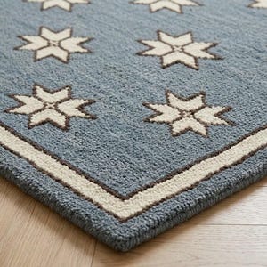 Könnte beinhalten: Ein blauer Teppich mit einem wiederkehrenden Muster aus weißen achtstrahligen Sternen mit dunkelbraunen Umrandungen. Der Teppich hat einen dicken, strukturierten Flor und einen breiten, cremefarbenen Rand, der das Sternmuster einrahmt.
