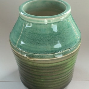 May include: A handcrafted ceramic vase with a wide, open top and a rounded, textured body. The vase features a gradient of green hues, transitioning from a lighter shade at the top to a darker tone at the base. The rim is a lighter shade of green.