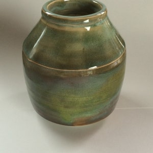May include: A handcrafted ceramic vase with a wide, rounded body and a narrow opening. The vase features a glossy finish with shades of green, brown, and blue. A horizontal band encircles the middle of the vase. The vase is suitable for home decor.