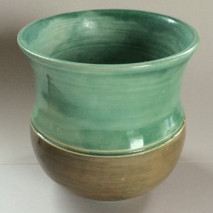 May include: A handcrafted ceramic vase with a two-tone design. The upper portion is a glossy, light teal color, while the lower section is a matte, earthy brown. The vase has a rounded base and a slightly flared rim, suitable for displaying flowers or as a decorative piece.