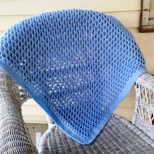 May include: A light blue crocheted baby blanket with a delicate openwork pattern. The blanket is draped over a white wicker chair.