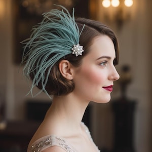 May include: A vintage-style hair accessory featuring a cluster of pale blue feathers and a pearl and rhinestone embellishment. The hairpiece is secured with a small pin and adds a touch of elegance to any hairstyle. Perfect for weddings or special events.