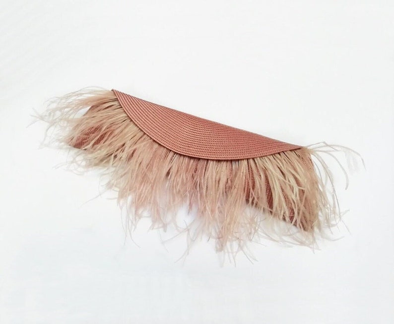 May include: A blush pink clutch with a woven straw base and a feathered trim.