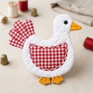Peut inclure: Un ornement en tissu matelassé en forme de poule avec un corps blanc, une queue et une aile à motif vichy rouge et blanc. La poule possède un bec et des pattes jaunes, ainsi qu'un petit œil en bouton noir. Le design est plat et surpiqué.