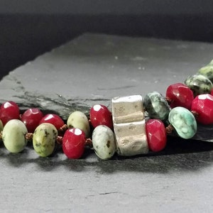 May include: A multi-strand bracelet with red and green gemstone beads and a silver spacer bead.